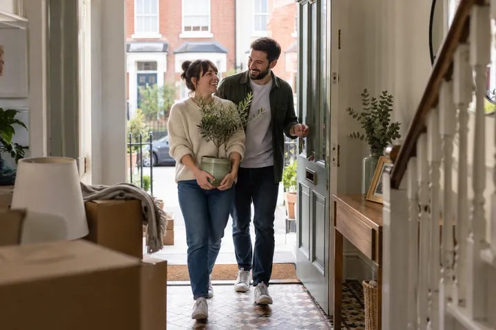 A couple arriving at a new home with a potted plant